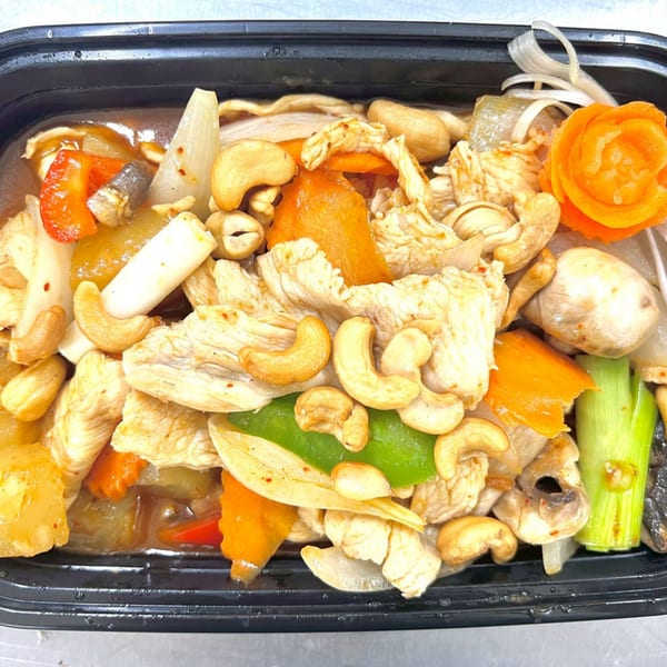 Thai cashew chicken with vegetables, including carrots, onions, and mushrooms, in a black takeout container.