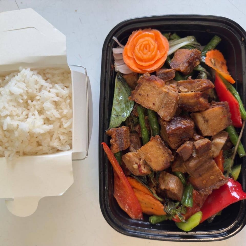 Thai crispy pork belly with vegetables and a side of white rice in takeout containers.