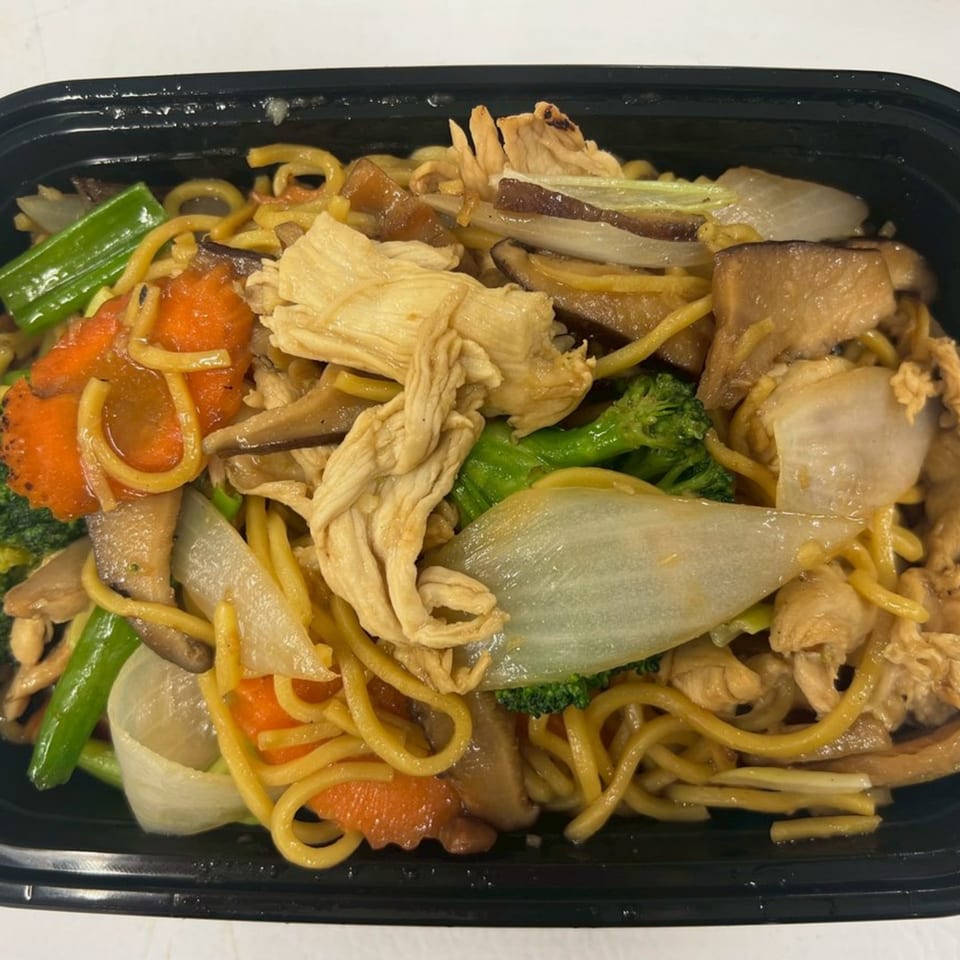 Thai noodles with chicken, broccoli, carrots, onions, and mushrooms in a black takeout container.