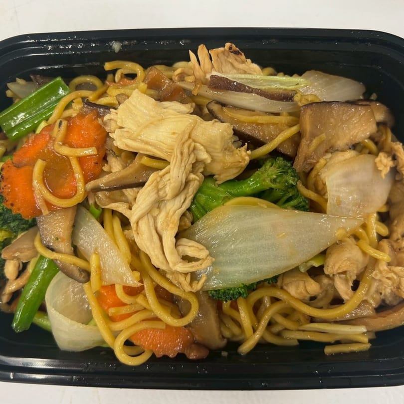 Thai noodles with chicken, broccoli, carrots, onions, and mushrooms in a black takeout container.
